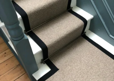close-up-og-bage-and-black-stair-runner-on-white-stairs-next-to-blue-wall
